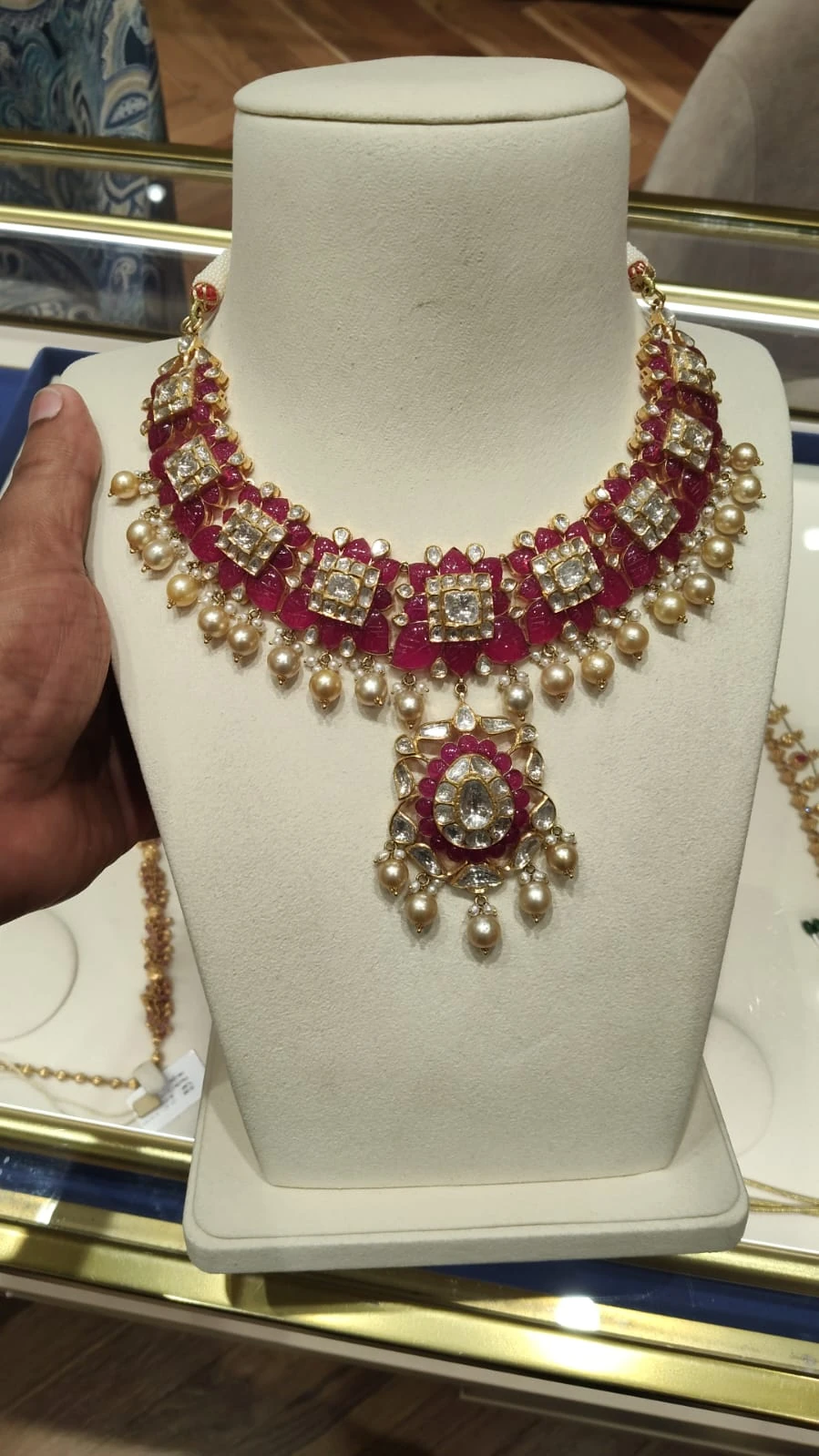 Raw in-store phone photo of a ruby-and-pearl necklace on a display bust